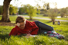 A student reads a book in the grass on IU Bloomington's campus.